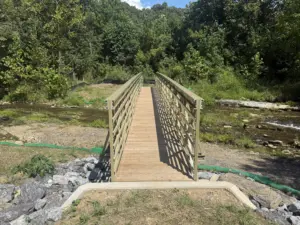 Completed olive-green FRP pedestrian truss bridge with timber decking spanning rocky Catawba Creek on the Andy Layne Trail, framed by a forested hillside.