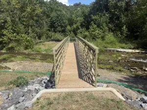 Completed olive-green FRP pedestrian truss bridge with timber decking spanning rocky Catawba Creek on the Andy Layne Trail, framed by a forested hillside.