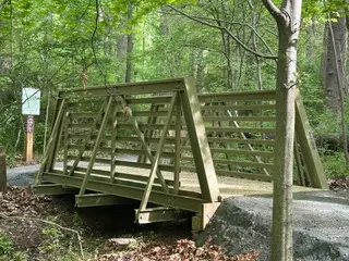 Side view of an olive green FRP truss bridge spanning a natural gap in a wooded environment.
