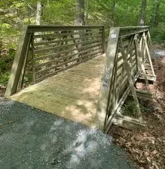 Angled approach view of an FRP truss bridge highlighting the pressure-treated yellow pine flooring and sloped ends.